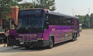 Photograph of a Bustang charter bus parked next to a side walk. A woman with a suitcase appears to have just gotten of the bus.