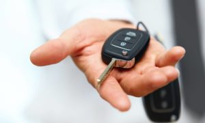 Photograph of an open hand holding car keys and the arm appears to be extended towards the camera.