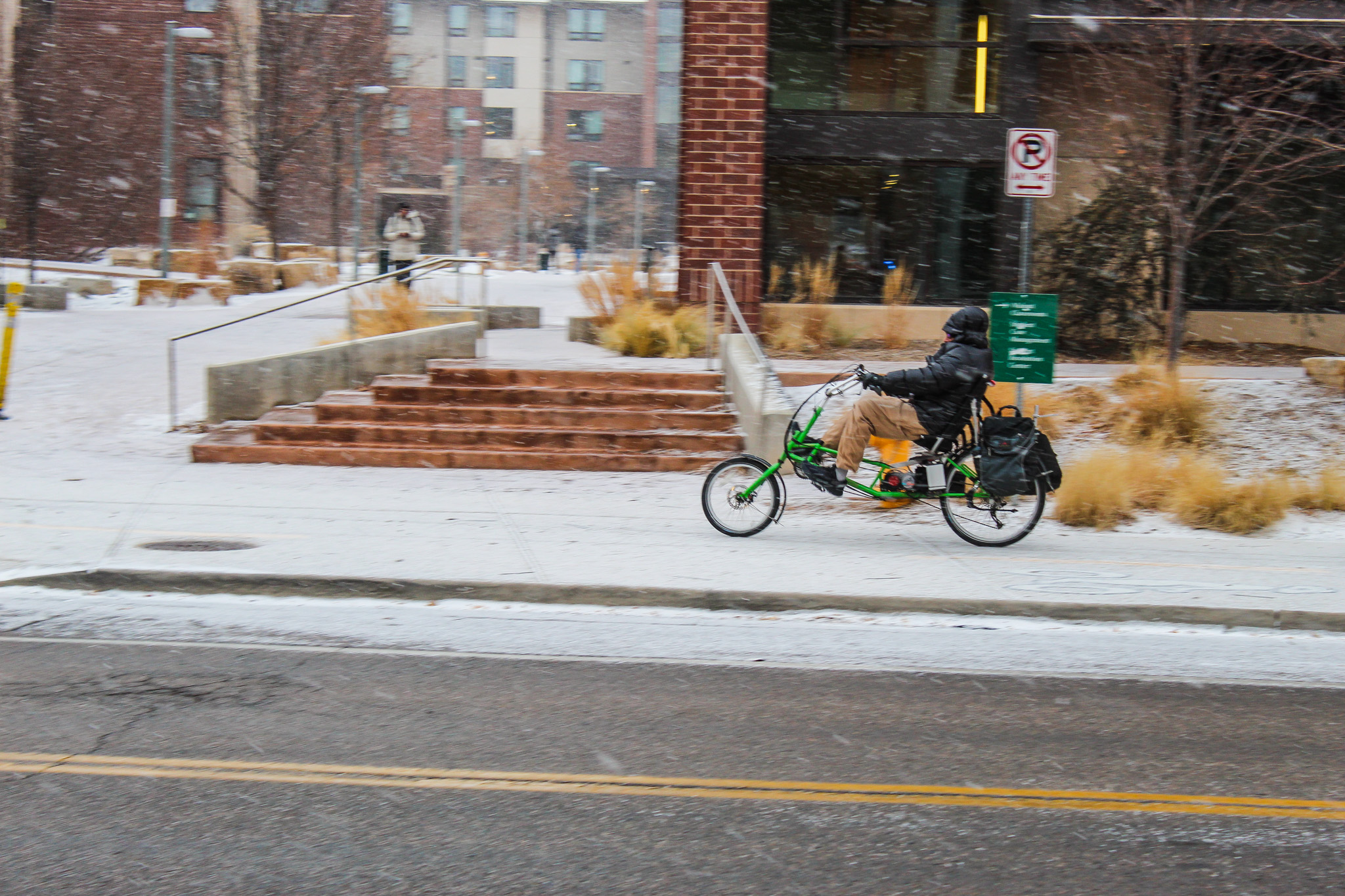 On a snowy day, a man bikes on a reclining bike.